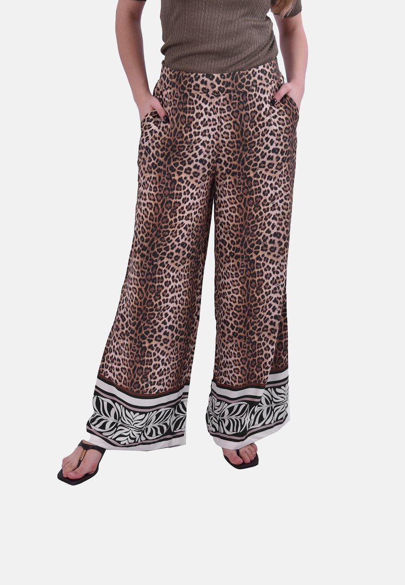 Pantalon large à imprimé léopard avec ourlets à motifs noirs et blancs, porté avec un haut marron et des sandales noires.