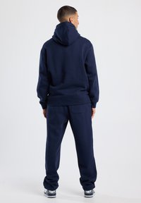 Conjunto de sudadera con capucha y pantalones de chándal en azul marino, fabricado en una mezcla de algodón, con capucha ajustable, puños acanalados y bolsillos laterales. Color sólido y sencillo.