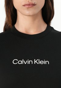 Zwart katoenen t-shirt met een ronde hals en korte mouwen, met "Calvin Klein" in het wit gedrukt, gecentreerd over de borst.