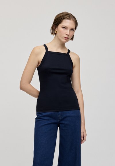 Top negru ajustat cu decolteu pătrat și bretele subțiri. Textură netedă, asociat cu blugi evazați de culoare albastru închis. Design minimalist.