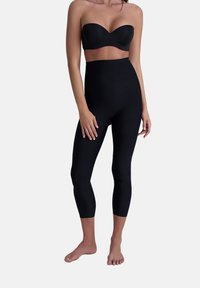 Leggings neri a vita alta realizzati in materiale morbido, con una silhouette aderente e taglio alla caviglia. Indossati con un top senza spalline.