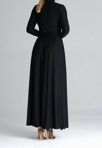 Zwarte maxi-jurk met lange mouwen, een getailleerde taille, zachte stof en een vloeiende rok, gecombineerd met doorzichtige hoge hakken.