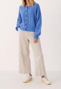 Stickad blå cardigan med kabelmönster, försedda med knappar fram. Kombineras med ljusbeige kordbyxor och vita sneakers.