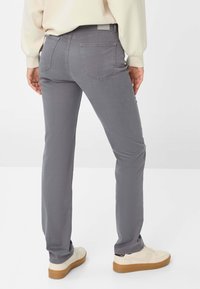 Pantalons en denim gris extensible avec une coupe slim, poches arrière et taille mi-haute, associés à des baskets blanches et un haut beige clair.