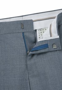 Grå texturerade byxor med dragkedja, kontrasterande blå dragkedja och vitt foder med randiga accenter.