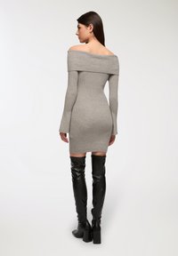 Abito grigio a coste con spalle scoperte e maniche fitted lunghe, abbinato a stivali neri in pelle al ginocchio con tacchi robusti.