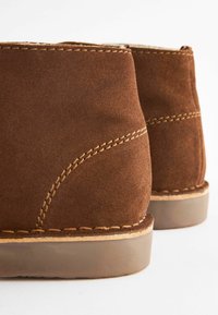 Ruske nubuk ankle kengät sisältävät ommeltua muotoilua, pyöreää muotoa ja paksua vaaleanruskeaa kumipohjaa. Pintamateriaali on pehmeä ja matta.