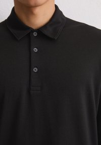Zwarte poloshirt gemaakt van een fijne katoenmix, met een kraag, een knoopsluiting met drie knopen en een ingetogen ontwerp zonder patronen.