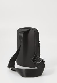 Sac à bandoulière noir, rectangulaire, en matériau lisse, avec fermeture éclair et bandoulière réglable. Design minimaliste sans embellissements.