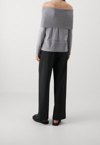 Maglione grigio a spalle scoperte, texture a coste, design senza cuciture, maniche lunghe, abbinato a pantaloni neri a gamba larga e sandali piatti.