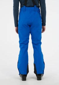 Blauwe skibroek met verstelbare zwarte bretels, heeft een relaxed fit, ritsventilatie aan de zijkant, en zwarte accenten op de onderbenen.