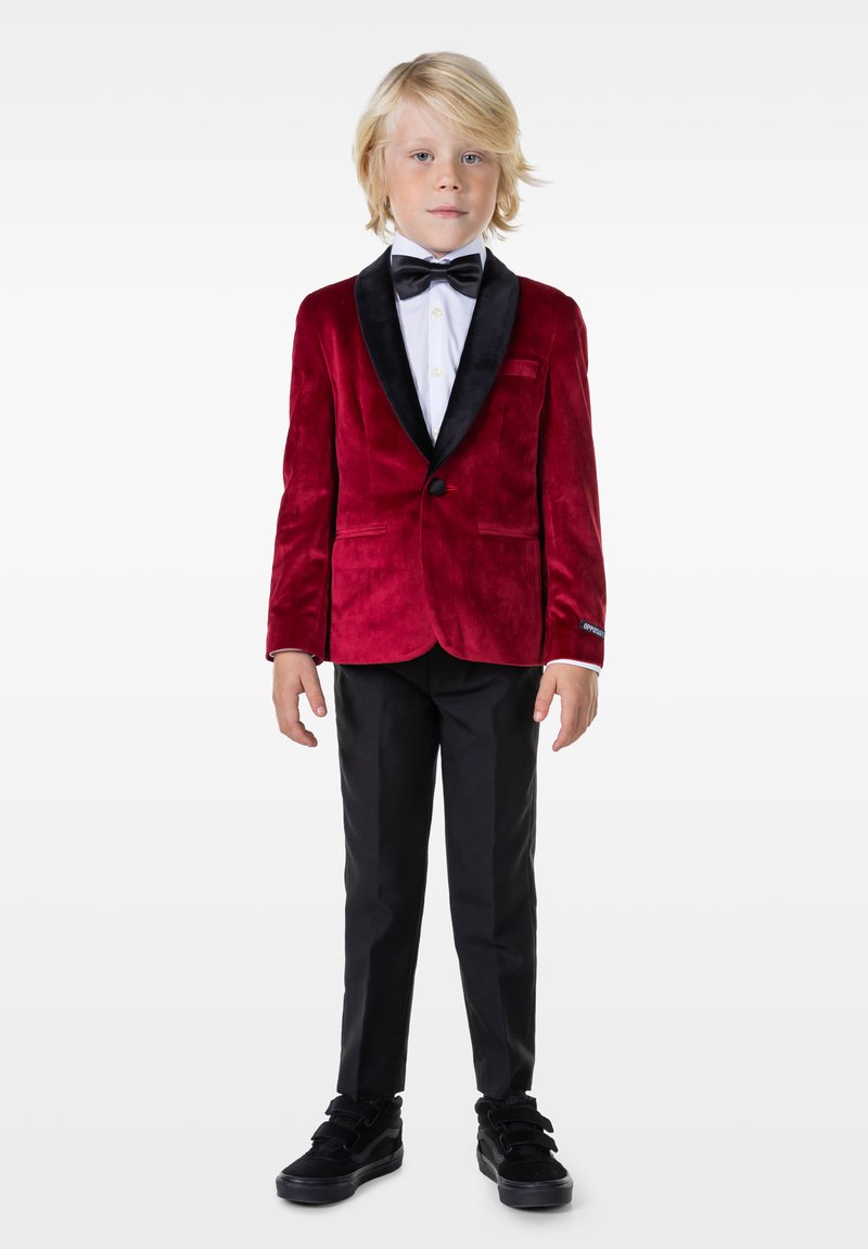Blazer de terciopelo rojo con solapas de satén negro, combinado con una camisa de vestir blanca, pajarita negra y pantalones y zapatos de vestir negros.