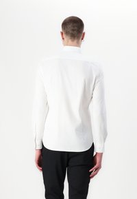 Weißes Langarmhemd aus glattem Stoff, mit einem spitzen Kragen, Knopfmanschetten und abgerundetem Saum. Zeigt die Rückansicht mit minimalen Details.