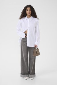Λευκό πουκάμισο με κουμπιά και μακριά μανίκια, συνδυασμένο με γκρι παντελόνι φαρδύ στο πόδι και μικρή καφέ τσάντα με διάτρητες λεπτομέρειες. Λευκά μυτερά παπούτσια.