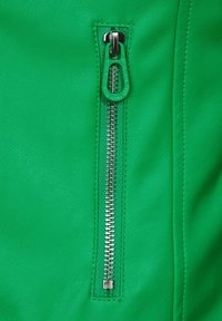 Tissu en cuir vert avec une fermeture éclair en métal argenté dotée d'une tirette verte, mettant en valeur une texture lisse et des détails de couture marquants.
