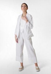 Blazer bianco in lino e pantaloni a gamba larga con un top in maglia a coste testurizzata. Sneakers beige completano l'outfit. Collana di perline verdi come accento.