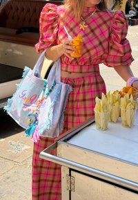Personne en tenue à carreaux rose tenant une tasse de tranches de mangue près d'un chariot avec des tasses de fruits tranchés dans une rue ensoleillée.