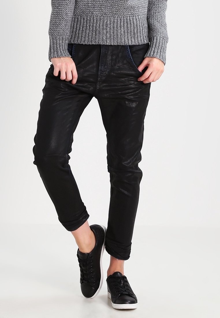 Černé kalhoty s koženým vzhledem a zúženým střihem, s předními kapsami a dekorativním šitím. Kombinované s černými teniskami a šedým pleteným svetrem.