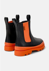 Bottines noires en cuir avec un panneau élastique orange, semelle texturée et semelle extérieure chunky orange. Équipées de boucles en onglet pour un enfilage facile.