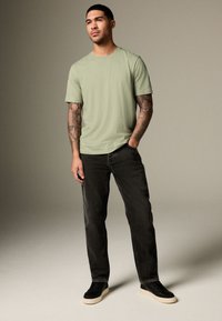 Svetlo zelena bombažna majica s klasičnim okroglim izrezom, kombinirana s črnimi jeans hlačami in črnimi supergami z belim podplatom.