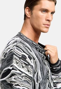 Textureret sort-hvid pullover med intrikate mønstre, struktureret krave og lagdelte stofdetaljer. Fremstillet af strikket materiale.