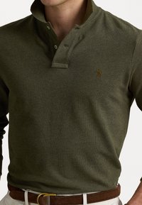 Olive green long-sleeve polo shirt with a buttoned collar, textured fabric, and a small, embroidered logo on the chest.