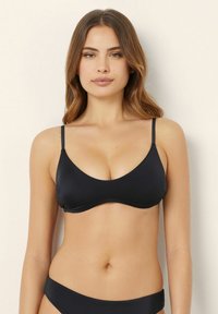 Svart bikiniöverdel i slät textil med justerbara tunna remmar, V-ringning och subtil textur, vilket ger ett enkelt och modernt utseende.