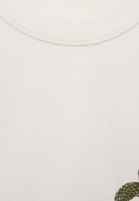 Witte katoenen t-shirt met ronde hals, met een gestructureerd groen patroon aan de onderrechte kant. Glad materiaal met minimale stikdetails.