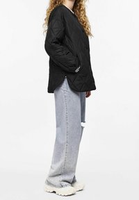 Black quilted jacket with a diamond pattern, featuring a rounded hem and side pockets. Worn over light blue distressed jeans and chunky white sneakers.
