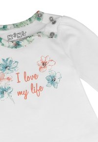 Biała koszulka dla niemowlaka z kwiatowym nadrukiem i napisem "Kocham moje życie" w kolorze koralowym, z zatrzaskami na jednym ramieniu i zielonym wykończeniem kołnierzyka.