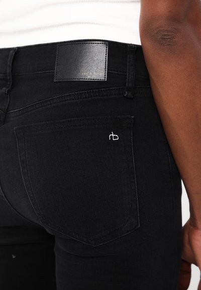 Jeans negre din denim cu o textură netedă, având o etichetă din piele pe talie și un mic logo brodat pe buzunarul din spate.