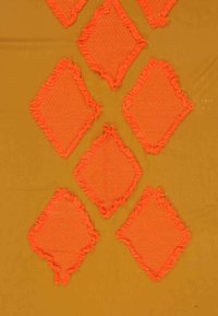 Seitsme oranžist rombikujulist kudumistükki, millel on kiilukesed servad, on paigutatud vertikaalsesse mustrisse sinepikollasel taustal.