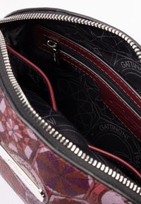 Wnętrze torby z teksturowanej tkaniny w głębokim burgundzie z czarnymi geometrycznymi wzorami. Zawiera kieszeń na zamek błyskawiczny oraz kontrastowe skórzane akcenty. Srebrny zamek.