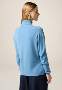 Maglione a collo alto azzurro chiaro con una consistenza morbida, maniche lunghe e una vestibilità rilassata, abbinato a pantaloni in denim scuro.
