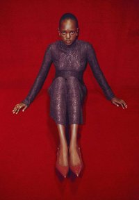 Mono de encaje en púrpura oscuro, ajustado al cuerpo y con mangas largas. Combinado con tacones rojos de punta. El fondo presenta un color rojo sólido.