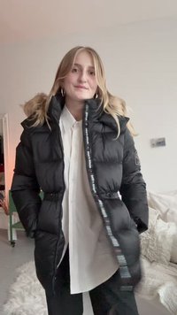 Czarna kurtka puchowa z wysokim kołnierzem, zapięciem na zamek błyskawiczny i bocznymi kieszeniami; posiada kaptur wyłożony futrem oraz akcenty logo na taśmie zamka.