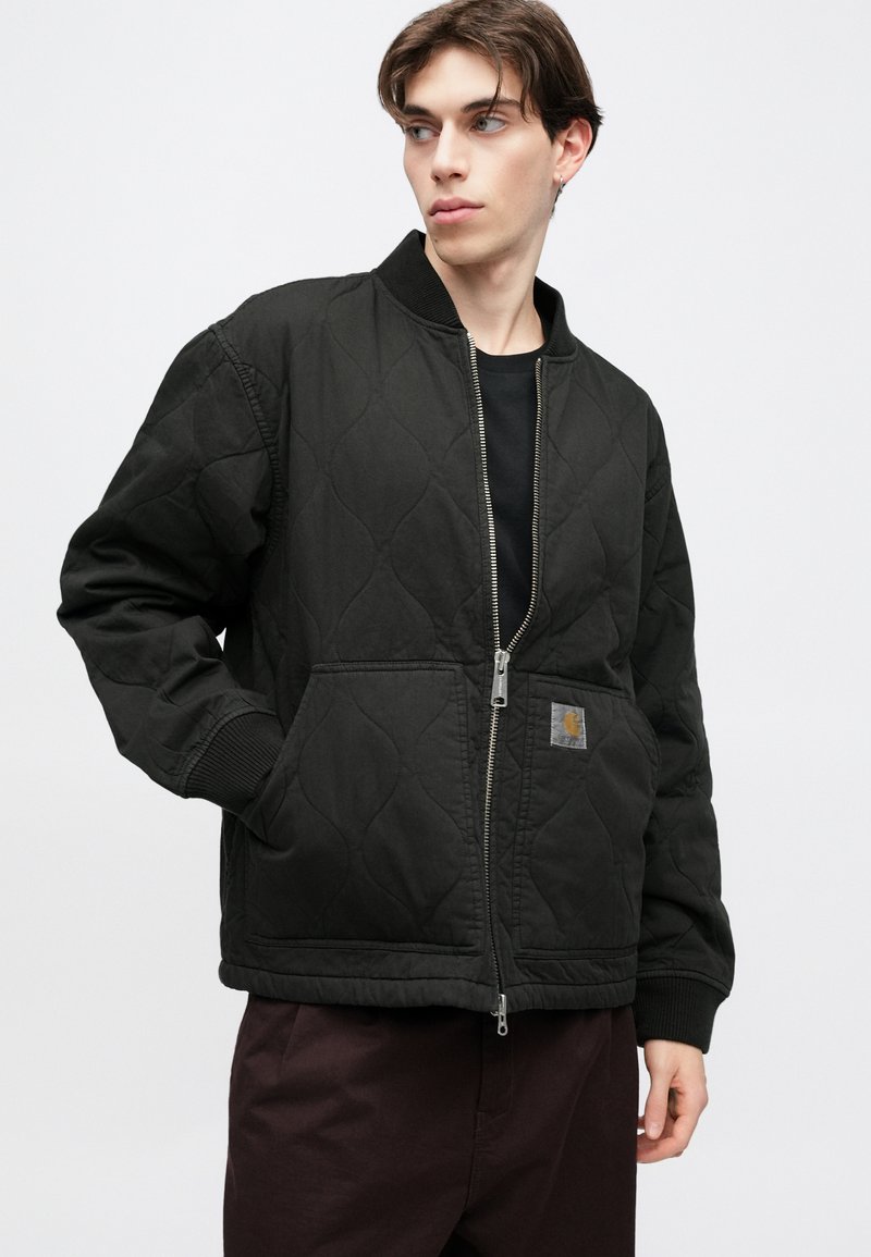 Black quilted bomber jacket with ribbed cuffs and collar. Features a front zip closure and a small logo patch on the left pocket.
