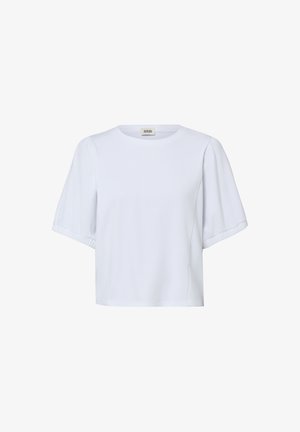 Blouse blanche à manches courtes avec encolure ronde et manches légèrement bouffantes, confectionnée en tissu lisse, présentée sur un fond uni.