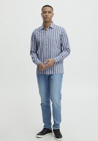 Gestreepte, langärmelige overhemd met knopen in blauw en wit, gecombineerd met licht denim jeans en zwarte sneakers. Opvallende zakdetail op het overhemd.