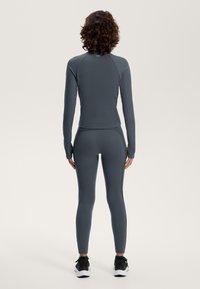 Tvådelat sportset i mörkgrått, bestående av en långärmad topp och leggings med tajt passform och texturerat tyg. Accentdetaljer på sidorna.