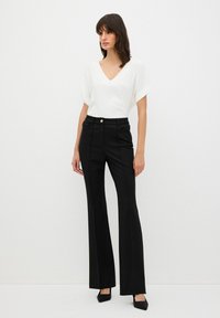 Witte v-hals blouse met opgerolde korte mouwen, gecombineerd met hooggetailleerde zwarte flared broeken met een voorste knoop en gestructureerd design.