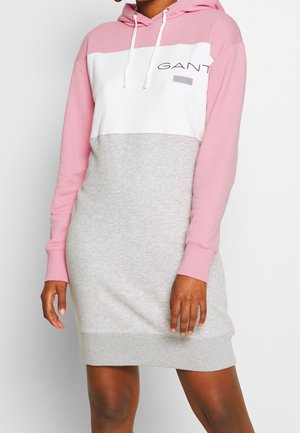 Femme portant une longue robe à capuche color block aux manches roses, panneau blanc sur la poitrine et partie jupe grise arborant un logo GANT sur la poitrine.