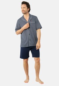 Chemise de pyjama à manches courtes à carreaux navy avec des finitions blanches et une poche, accompagnée de shorts navy unis. Tissu doux, coupe décontractée.
