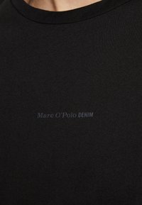 Svart kortermet t-skjorte laget av glatt bomull, med rund hals og subtil merkevare "Marc O'Polo DENIM" i grå.