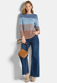 Maglione lavorato a maglia con righe orizzontali in blu e marrone, abbinato a jeans a gamba larga blu. La modella tiene una borsa a tracolla color sabbia. Stivaletti beige.