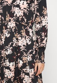 Floral dress in black fabric featuring pink, beige, and burgundy floral patterns; long sleeves with elastic cuffs, gathered waist, and soft texture.