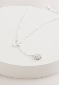 Silver necklace featuring a heart-shaped pendant with a cluster of clear crystals, set on a fine chain with a small heart charm.