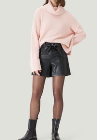Helles rosa, oversized Sweatshirt mit umgeschlagenem Kragen, kombiniert mit hoch taillierten schwarzen Leder-Shorts mit Bindegürtel. Schwarze Ankle Boots.