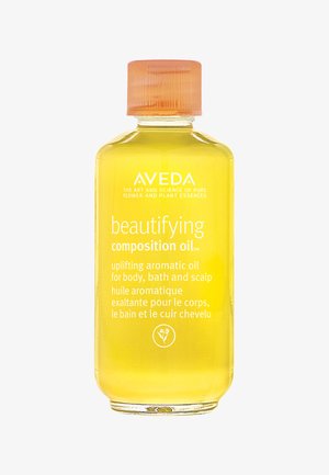 L'huile de composition embelissante Aveda dans une bouteille en verre transparent. L'huile est d'un jaune vif, avec un capuchon orange strié et des étiquettes blanches.