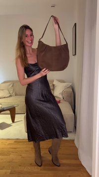 Καφέ σουέντ τσάντα χόμπος με κοντό λουρί ώμου, με απαλή υφή και στρογγυλεμένο σχήμα, κρατιέται από άτομο που φοράει μαύρο σατέν φόρεμα.